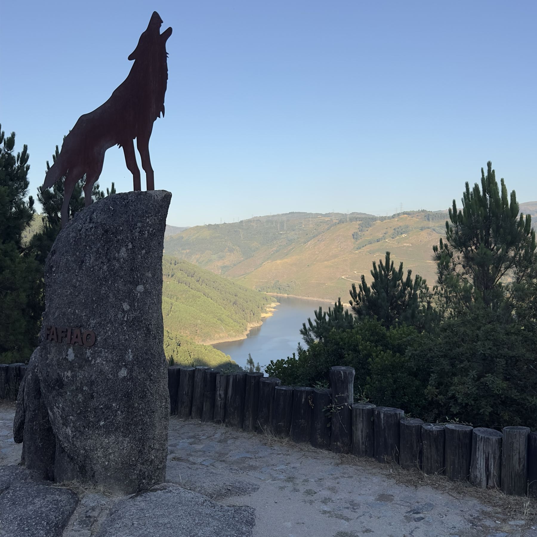 Escultura de um lobo a uivar sobre um marco de granito com a inscrição Fafião, com a albufeira ao fundo